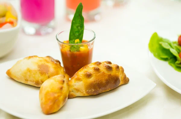 Apetizer of small tomato soup in shotglass and delicious mini empanadas spread around on white plate — Stock Photo, Image
