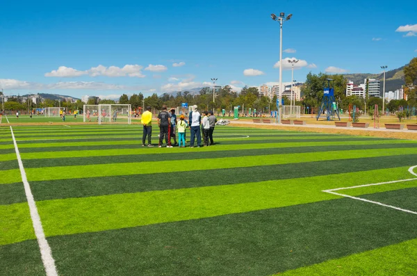 QUITO, ECUADOR - 8 AUGUST, 2016: Группа людей, стоящих на футбольном поле, расположенном в центре городского парка Ла Каролина, искусственная зеленая трава поверхность, здания видимый фон, красивый солнечный день — стоковое фото