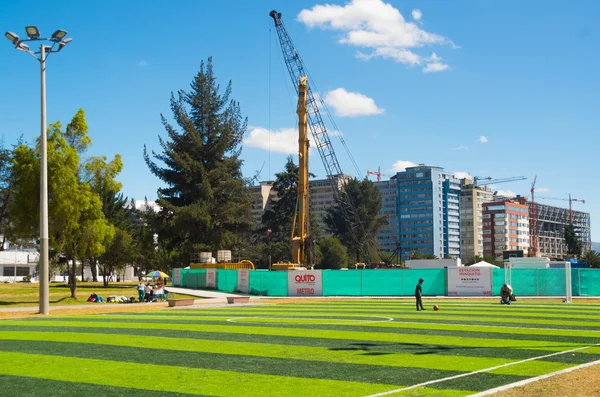 Quito, Ecuador - 8 augusti 2016: grön artificiell fotboll fält i innerstaden park La Carolina, med stora konstruktion kran i bakgrunden, vacker solig dag — Stockfoto