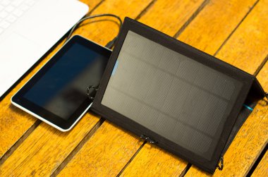 Taşınabilir güneş şarj dizüstü bilgisayar ve tablet yanında ahşap yüzey üzerinde oturan, yukarıdan görüldüğü gibi, modern teknoloji kavramı