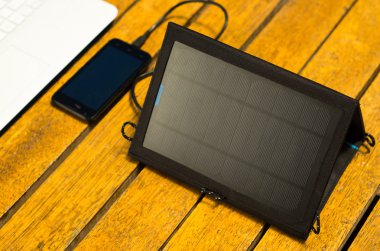 Taşınabilir güneş şarj dizüstü bilgisayar ve cep telefonu yanında ahşap yüzey üzerinde oturan, yukarıdan görüldüğü gibi, modern teknoloji kavramı
