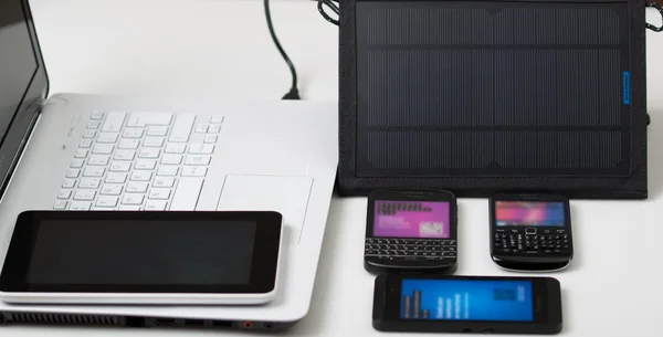 Nice black portable solar charger and tablet sitting next to exclusive white laptop, three mobile phones on desk also, modern business technology concept, studio background