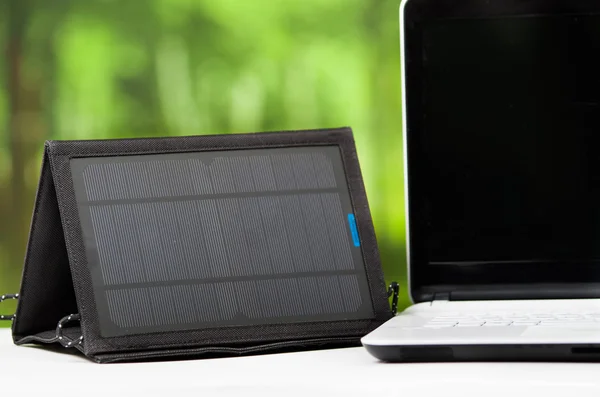 Přenosná solární nabíječka, která sedí na dřevěné ploše vedle přenosného počítače, jak je vidět shora, koncepce moderního technického vybavení — Stock fotografie