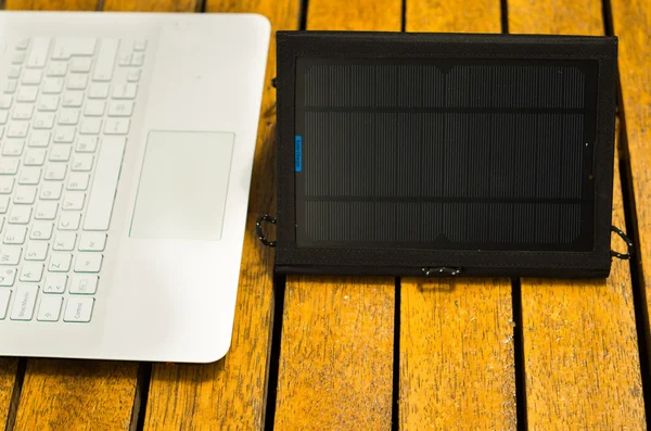 Portable solar charger sitting on wooden surface next to laptop computer, as seen from above, modern technology concept — Stock Photo, Image