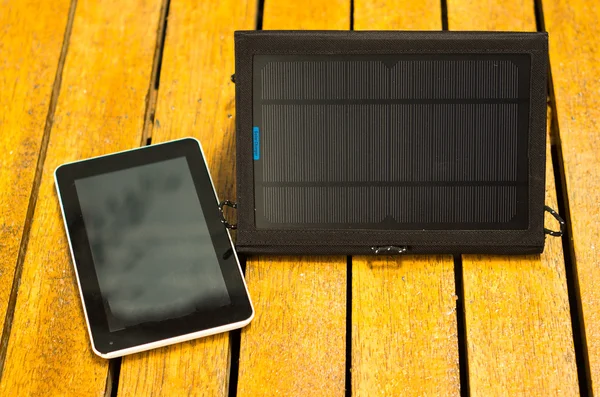 Portable solar charger sitting on wooden surface next to tablet, as seen from above, modern green technology concept — Stock Photo, Image