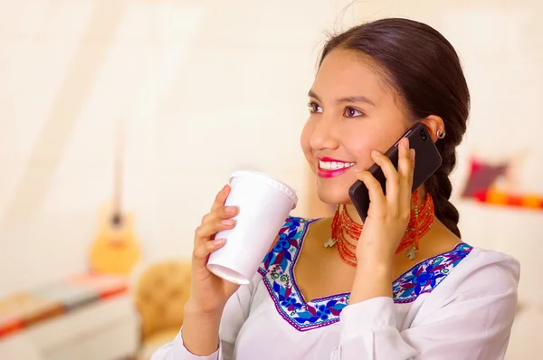 Retrato mujer bastante joven con blusa andina tradicional, sosteniendo taza de café blanco y hablando por teléfono móvil sonriendo — Foto de Stock