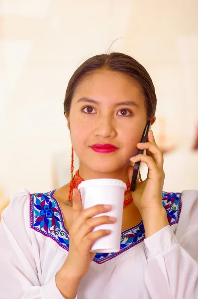 Portret mooie jonge vrouw dragen van traditionele Andes blouse, holding witte koffiemok en praten over mobiele telefoon glimlachend — Stockfoto