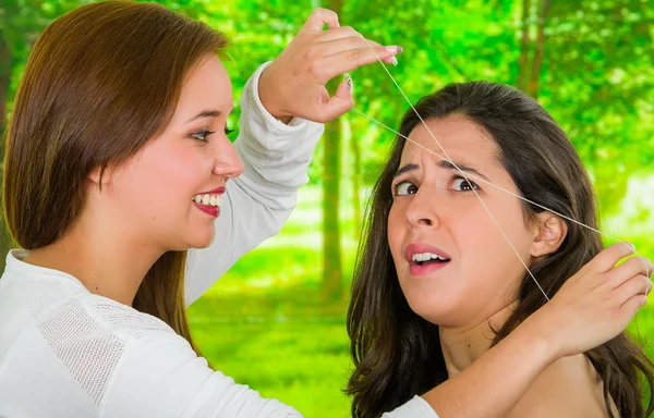 Mujer recibiendo depilación de cejas, mirada asustada en la cara, técnica de roscado realizada por profesionales con fondo de jardín — Foto de Stock