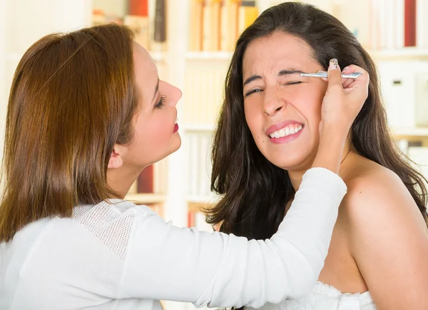 Donna che esegue la depilazione del sopracciglio usando pinzette sul viso dei clienti, espressioni facciali scomode, sfondo verde del giardino — Foto Stock