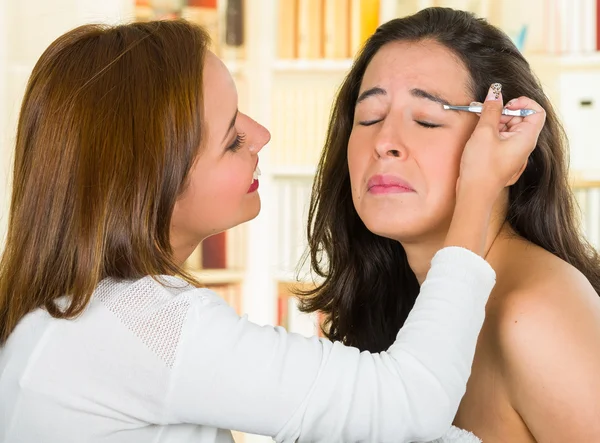 Mujer realizando depilación de cejas utilizando pinzas en la cara de los clientes, expresiones faciales incómodas, fondo de jardín verde — Foto de Stock