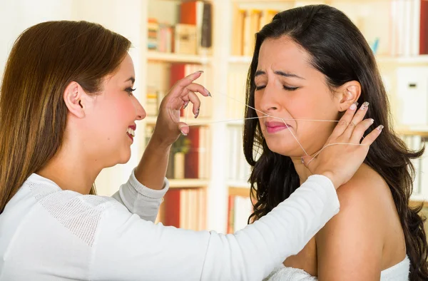 Cosmetoloog het uitvoeren van gezichts ontharing met behulp van threading techniek op brunette patiënt met pijnlijke gezichtsuitdrukkingen — Stockfoto