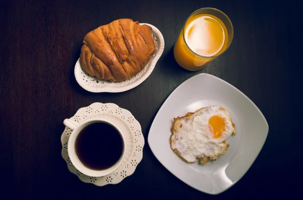 Menu du petit déjeuner tourné d'en haut, y compris une assiette de fromage et de beurre à côté de la tasse de café et du pain avec oeuf frit sur une surface en bois sombre — Photo