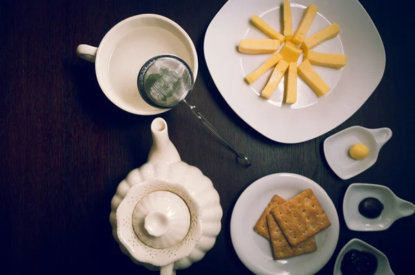 Teller mit Buiscuits und Käse, sternförmig auf dunkler Holzoberfläche neben Teekessel angeordnet, kleine Teller mit Marmelade und Butter, von oben geschossen — Stockfoto