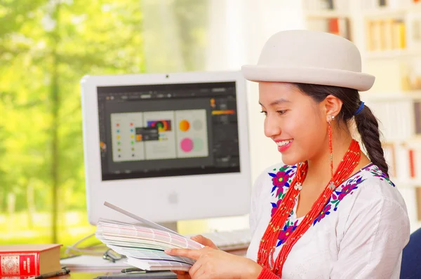 Menina bonita nova vestindo camisa branca e chapéu elegante, sentado à mesa do computador, virando-se para a câmera sorrindo alegremente — Fotografia de Stock