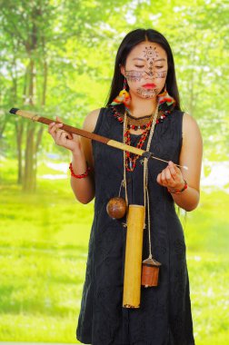 Amazon egzotik kadın, yüz boya, siyah elbise, oklar ve boyun etrafında asılı küçük ahşap şişe için durumda, ok zehir uygulayarak, poz, orman arka plan.