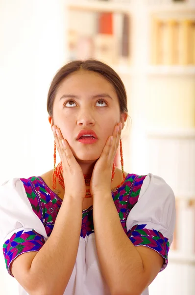 Hermosa mujer morena joven con blusa blanca andina tradicional con bordes decorativos azules, frente a la cámara interactina frustrado, fondo del hogar brillante — Foto de Stock