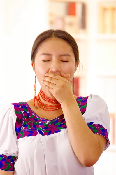 Hermosa joven morena vistiendo la tradicional blusa blanca andina con bordes decorativos azules, frente a la cámara interactuando cansado, brillante fondo del hogar — Foto de Stock