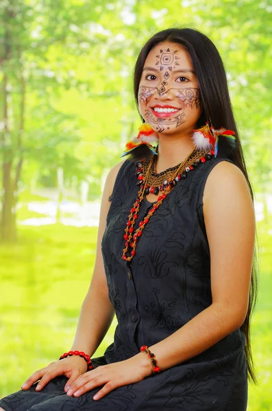 Ritratto donna esotica amazzonica con vernice facciale e vestito nero, posa orgogliosa per la macchina fotografica, sfondo della foresta . — Foto Stock