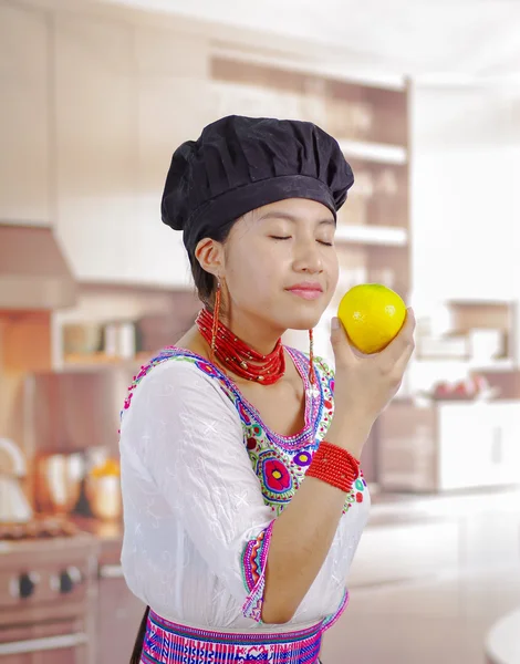 Young woman chef wearing traditional andean blouse, black cooking hat, holding up lemon for camera smiling, kitchen background — Stock Photo, Image