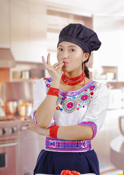 Jonge vrouw chef-kok met traditionele Andes blouse, zwarte kokende hoed, aanraken van lippen met vingers voor de camera, keuken achtergrond — Stockfoto