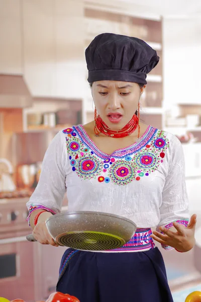 Jonge vrouw chef-kok met traditionele Andes blouse, zwarte kokende hoed, met koekenpan en kijken naar binnen met overstuur gezichtsuitdrukking, keuken achtergrond — Stockfoto