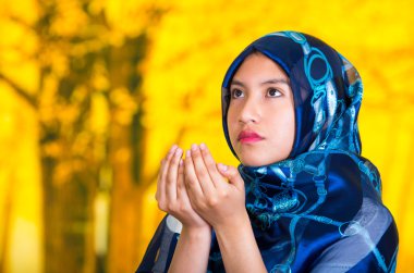 Mavi renkli başörtüsü takan güzel genç müslüman kadın, müslüman dua, sonbahar orman arka plan yapan el katlayarak kamera bakan