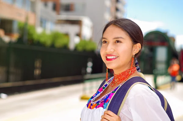 Mulher bonita vestindo blusa andina tradicional e mochila azul, à espera de ônibus na plataforma estação ao ar livre, sorrindo feliz — Fotografia de Stock