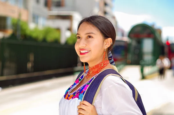 Mooie jonge vrouw dragen van traditionele Andes blouse en blauwe rugzak, wachten op bus op buiten station platform, glimlachend gelukkig — Stockfoto