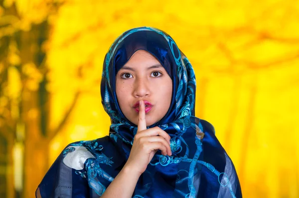 Vackra unga muslimska kvinnan bär blå färgad hijab, inför kameran poserar gör tystnad symbol röra läpparna med fingret, höst skogen bakgrund — Stockfoto