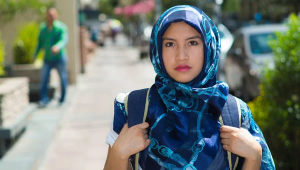 Mooie jonge moslim vrouw dragen blauw gekleurde hijab en rugzak, poseren met doordachte ernstige gezichtsuitdrukking in de straat, buitenshuis stedelijke achtergrond — Stockfoto