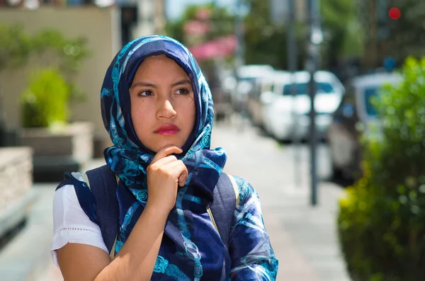 Bella giovane donna musulmana che indossa hijab e zaino di colore blu, in posa con riflessiva espressione facciale seria in strada, all'aperto sfondo urbano — Foto Stock