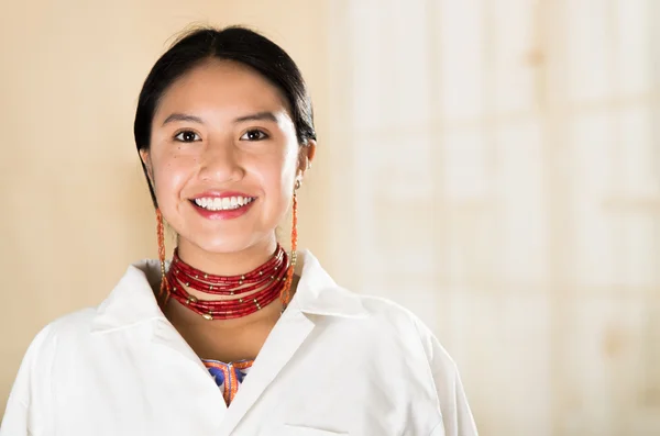 Jovem mulher bonita vestida de casaco de médicos e colar vermelho olhando para a câmera sorrindo, ovo branco clínica fundo — Fotografia de Stock