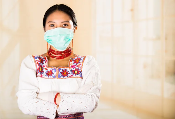 Mujer hermosa joven vestida con abrigo de médicos y collar rojo, cara cubierta con máscara facial mirando a la cámara, fondo de clínica clara de huevo — Foto de Stock