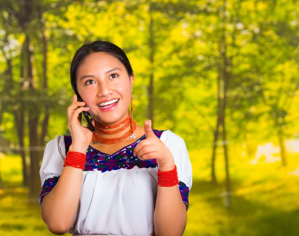 Mulher bonita vestindo blusa andina tradicional com colar, posando para câmera, segurando telefone celular falando, fundo verde floresta — Fotografia de Stock