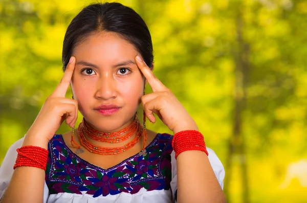 Cabeza hermosa mujer joven con blusa andina tradicional con collar rojo, posando para la cámara tocando la cara usando las manos mientras sonríe felizmente, fondo verde bosque — Foto de Stock