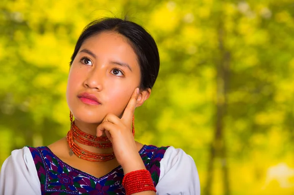 Headshot mooie jonge vrouw dragen van traditionele Andes blouse met rode ketting, poseren voor camera aanraken gezicht met de handen terwijl glimlachend gelukkig, groene bos achtergrond — Stockfoto