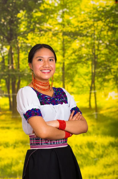 Piękna młoda kobieta noszenia tradycyjnych Andyjskiej bluzka z naszyjnik, stojąc pozuje do kamery, herb, skrzyżowane uśmiecha się radośnie, tło zielony las — Zdjęcie stockowe
