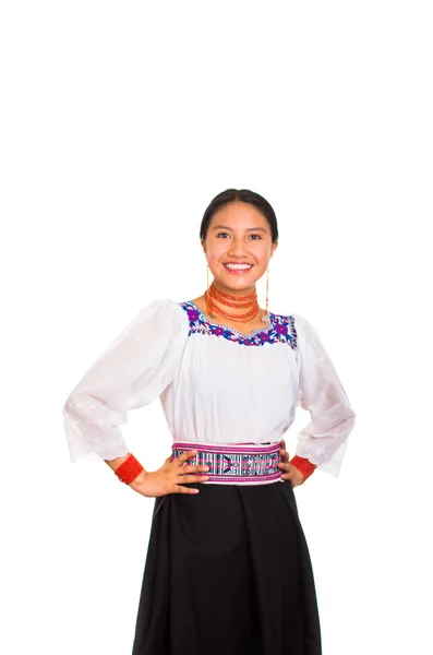 Beautiful young woman standing wearing traditional andean blouse and red necklace, holding arms on hips while smiling happily, white studio background — Stock Photo, Image