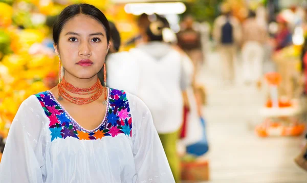 Bella giovane donna ispanica che indossa camicetta tradizionale andina in posa per la fotocamera all'interno del mercato della frutta, colorata selezione di alimenti sani in background — Foto Stock