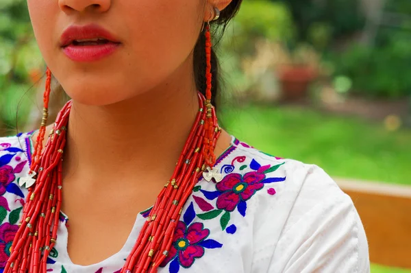 Feche a bela mulher hispânica vestindo blusa branca andina tradicional com decoração colorida ao redor do pescoço, combinando colar vermelho, pulseira e anel de orelha — Fotografia de Stock