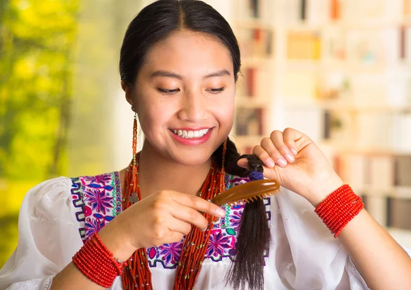 Hermosa mujer hispana usando blusa blanca con bordado colorido, usando un cepillo de pelo pequeño durante la rutina de maquillaje, fondo de jardín — Foto de Stock