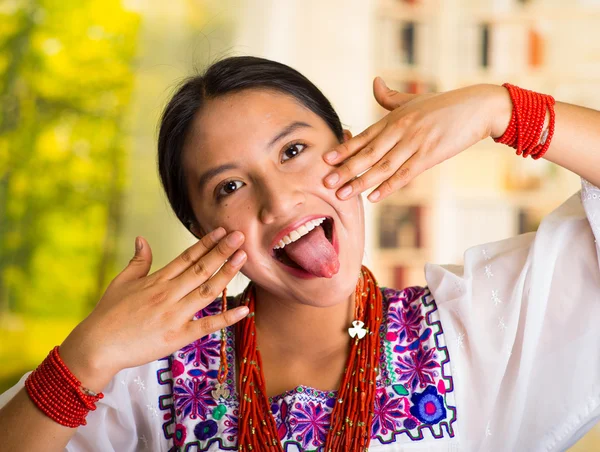 Schöne hispanische Frau trägt weiße Bluse mit bunten Stickereien, cremt das Gesicht mit beiden Händen beim Make-up, lächelt glücklich, Garten Hintergrund — Stockfoto