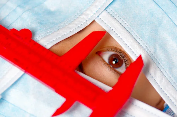 Ojo de cerca de la mujer asomándose desde la cubierta facial total, preparándose para el concepto de cirugía estética, médico utilizando la herramienta de medida roja — Foto de Stock