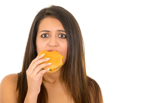 Ritratto bella giovane donna in posa per la macchina fotografica mangiare hamburger mentre rende colpevole espressione facciale, sfondo bianco studio — Foto Stock