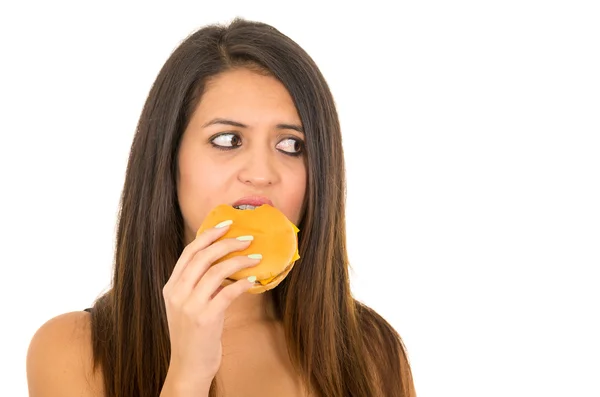 Portrait beautiful young woman posing for camera eating hamburger while making guilty facial expression, white studio background — Stock Photo, Image