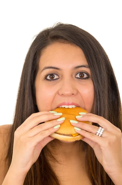 Portrait beautiful young woman posing for camera eating hamburger while making guilty facial expression, white studio background — Stock Photo, Image