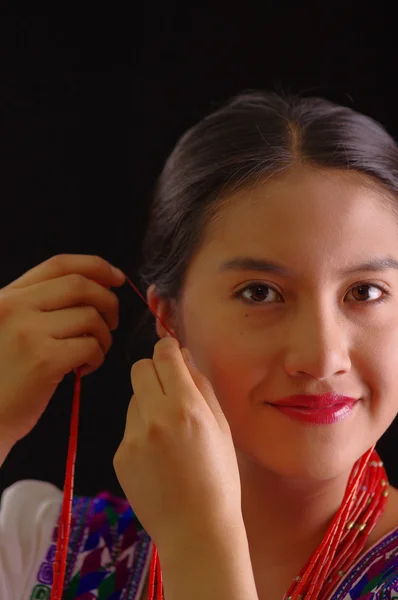 Όμορφη νεαρή ισπανίδα γυναίκα φορώντας λευκή μπλούζα με παραδοσιακές άκρες κέντημα, προσκολλώντας τα κόκκινα εξτένσιον η ίδια και χαμογελαστά, μαύρο στούντιο φόντο — Φωτογραφία Αρχείου