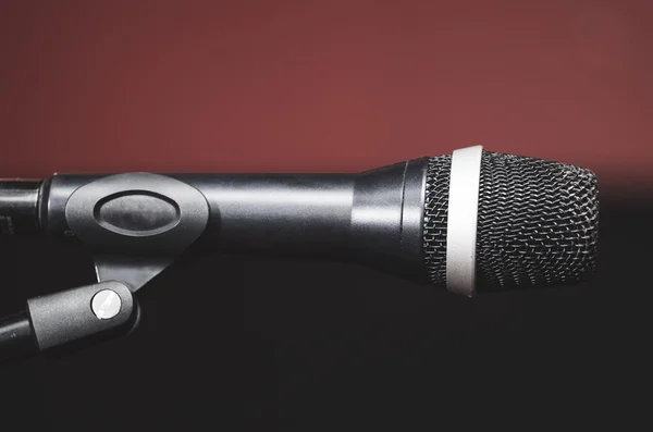 Gros plan microphone vocal noir monté sur support micro, fond de gâteau foncé rouge flou — Photo