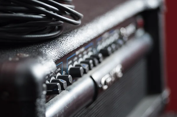 Closeup amplifier with row of buttons and knobs, descriptions turning blurry, cable bundle placed on top, studio equipment concept — Stock Photo, Image