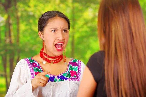 Two beautiful young women posing for camera, one wearing traditional andean clothing, the other in casual clothes, interacting argument, park background — Stock Photo, Image